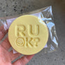 A packaged cookie with 'R U OK?' embossed on it, held in a person's hand.